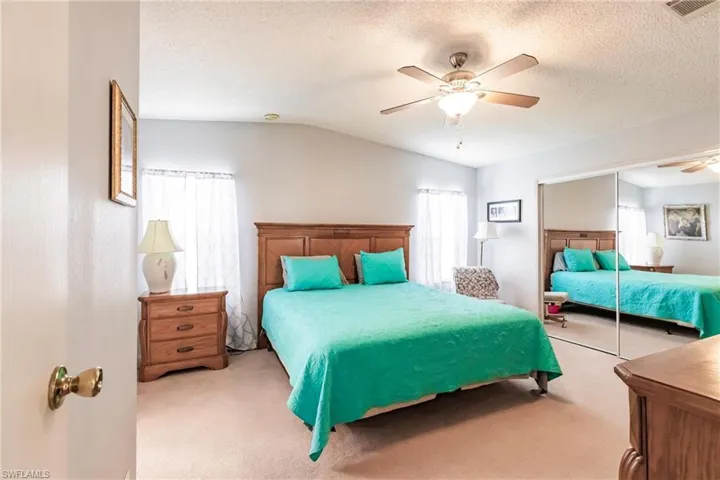 Carpeted bedroom with ceiling fan, a closet, vaulted ceiling, and a textured ceiling