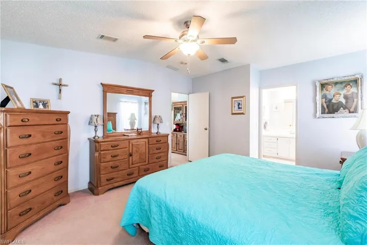 Carpeted bedroom featuring ceiling fan, a textured ceiling, lofted ceiling, and ensuite bath