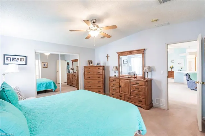 Bedroom with ceiling fan, vaulted ceiling, a textured ceiling, light carpet, and a closet