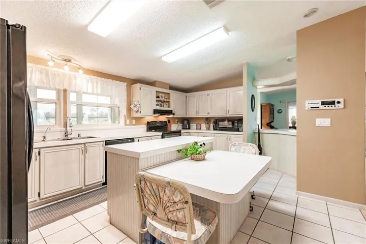 Kitchen with a center island, sink, black electric range oven, light tile patterned floors, and stainless steel fridge