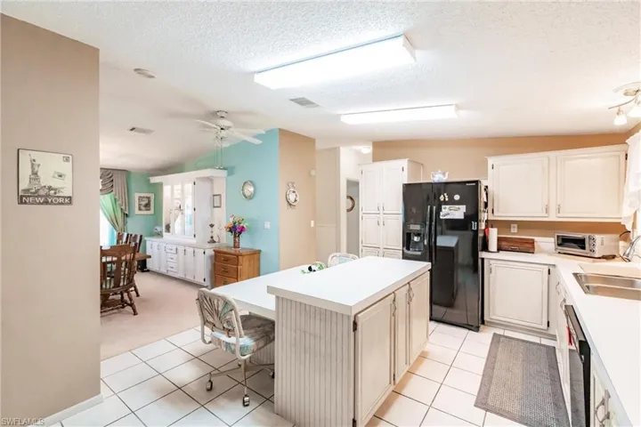 Kitchen with lofted ceiling, a kitchen island, black appliances, light tile patterned flooring, and a textured ceiling
