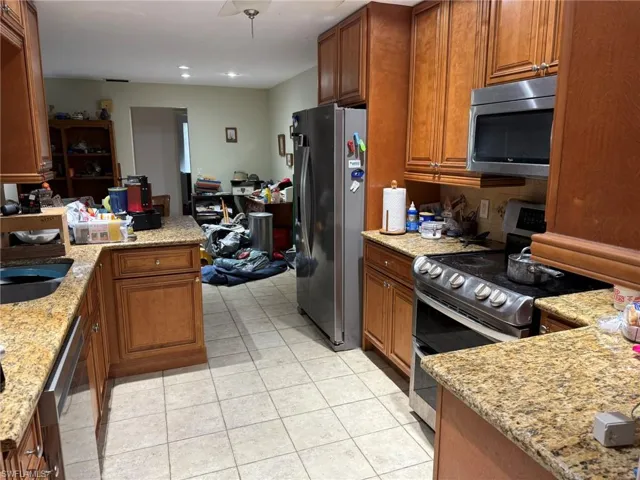 Kitchen featuring appliances with stainless steel finishes, brown cabinetry, light stone countertops, light tile patterned floors, and a peninsula