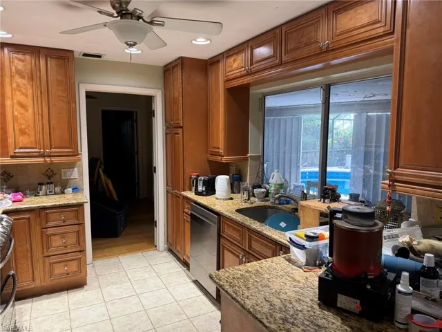 Kitchen with dishwasher, brown cabinets, light tile patterned flooring, light stone countertops, and recessed lighting