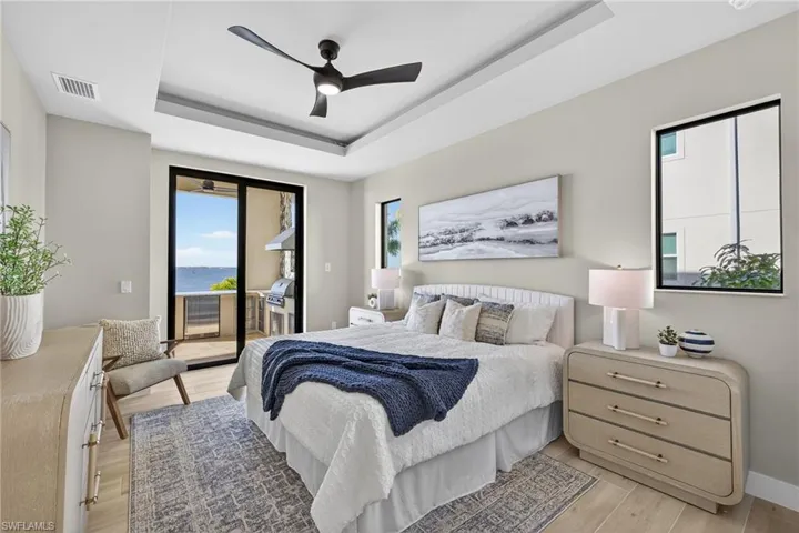 Bedroom with a water view, access to exterior, a raised ceiling, light wood finished floors, and a ceiling fan