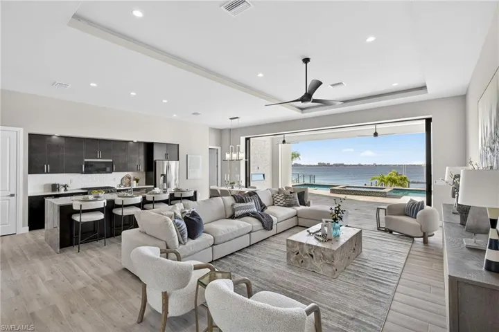 Living room featuring a water view, light wood-style floors, a ceiling fan, recessed lighting, and a tray ceiling