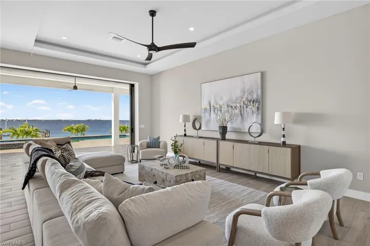 Living area with a water view, light wood-style floors, a ceiling fan, recessed lighting, and a raised ceiling