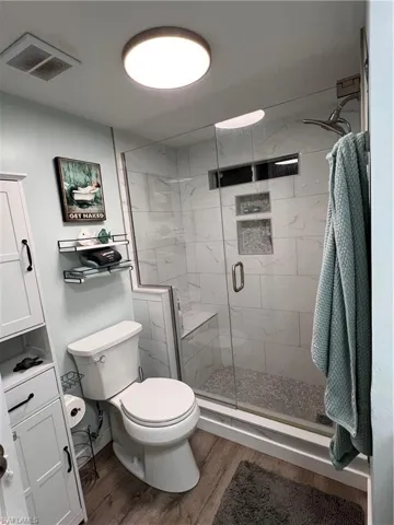 Full master bathroom featuring a stall shower and laminate floor, vent fan and led lighting