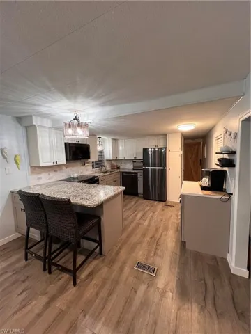Kitchen featuring granite countertops and peninsula, stainless steel appliances, tasteful backsplash, laminate floors, and separate coffee bar.