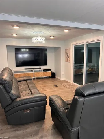 Living area with laminate floor with decorative ceiling light and fan combo, slider door access to screen-in porch, 80" mounted TV.