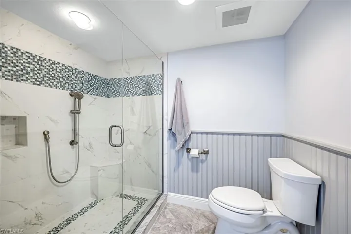 Bathroom with a marble finish shower, a wainscoted wall, and recessed lighting