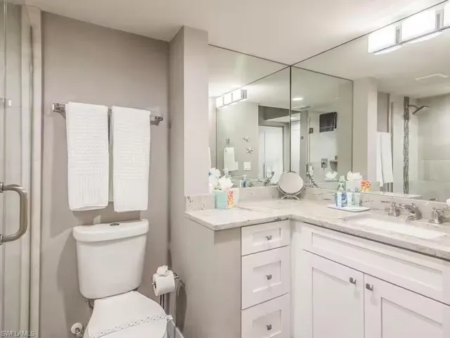 Bathroom featuring a light-colored vanity with a sink, reflective mirrored walls, and a toilet
