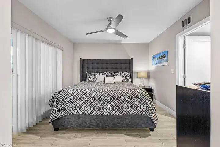 This sleeping area features light-toned flooring, a ceiling fan, and vertical blinds