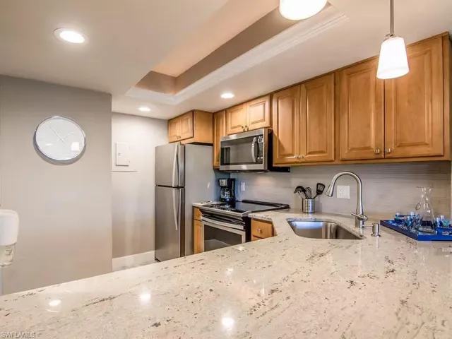 The kitchen features light-toned wooden cabinetry, stainless steel appliances, and a spacious countertop with a light-colored, speckled finish