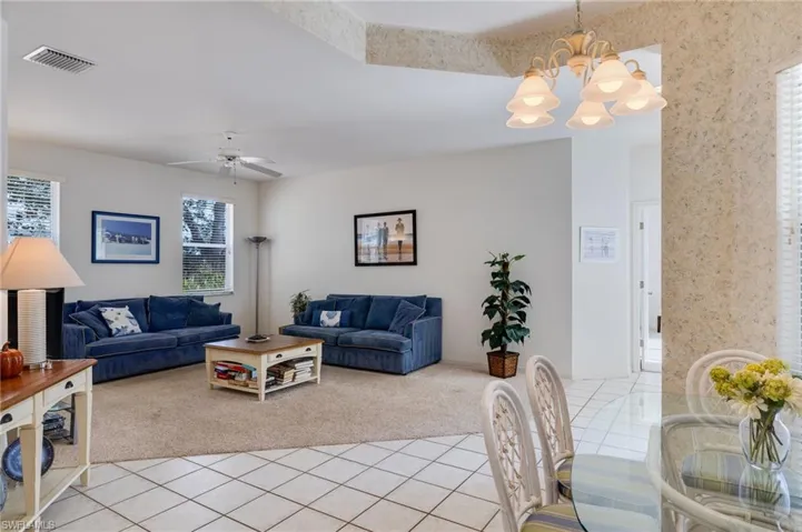 Living room with light tile patterned floors, light carpet, a chandelier, and a ceiling fan