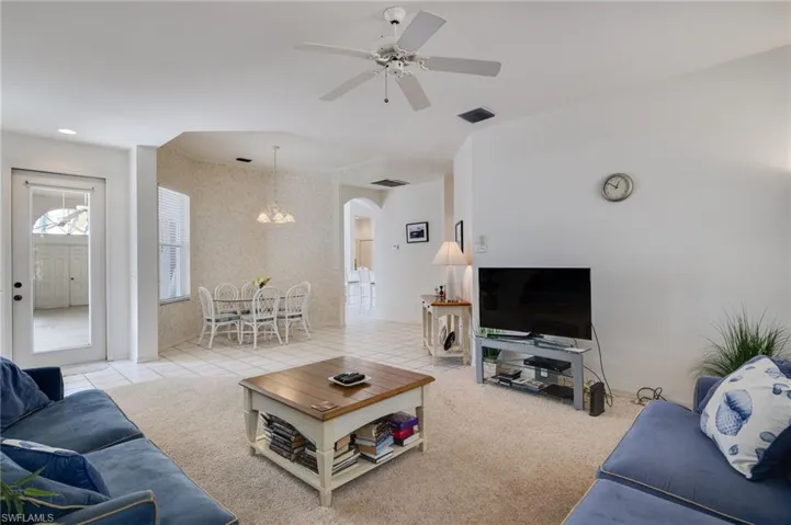 Living area featuring ceiling fan, light carpet, light tile patterned floors, and arched walkways