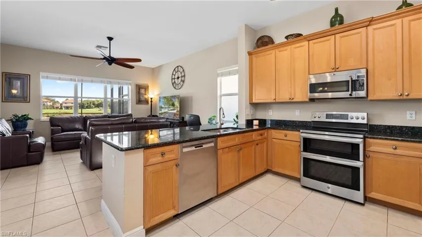 Kitchen featuring stainless steel appliances, a peninsula, light tile patterned floors, and dark stone countertops