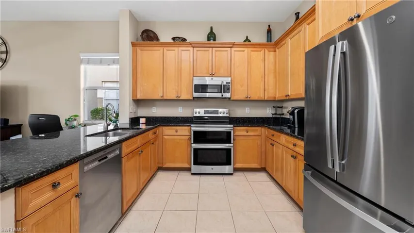 Kitchen featuring stainless steel appliances, dark stone counters, a peninsula, light tile patterned floors, and brown cabinetry