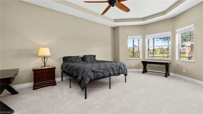 Bedroom with a tray ceiling, light carpet, and a ceiling fan