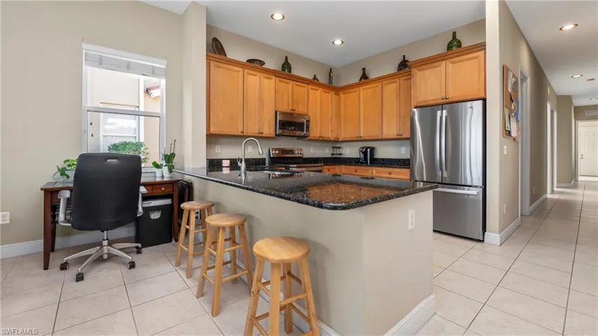 Kitchen featuring appliances with stainless steel finishes, dark stone countertops, a peninsula, light tile patterned flooring, and a kitchen bar
