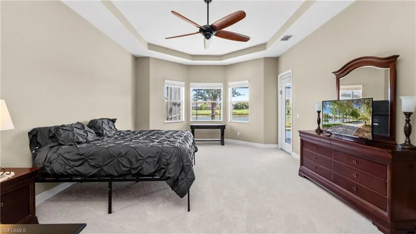 Bedroom featuring light colored carpet, a raised ceiling, access to outside, and ceiling fan