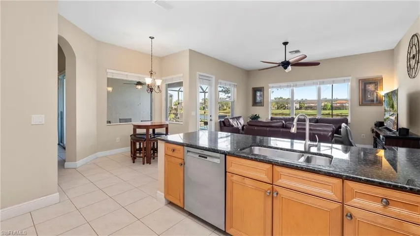 Kitchen with dishwasher, a ceiling fan, hanging light fixtures, dark stone countertops, and light tile patterned floors