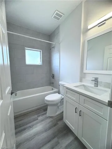 Full bathroom featuring tiled shower / bath, vanity, wood-type flooring, and toilet