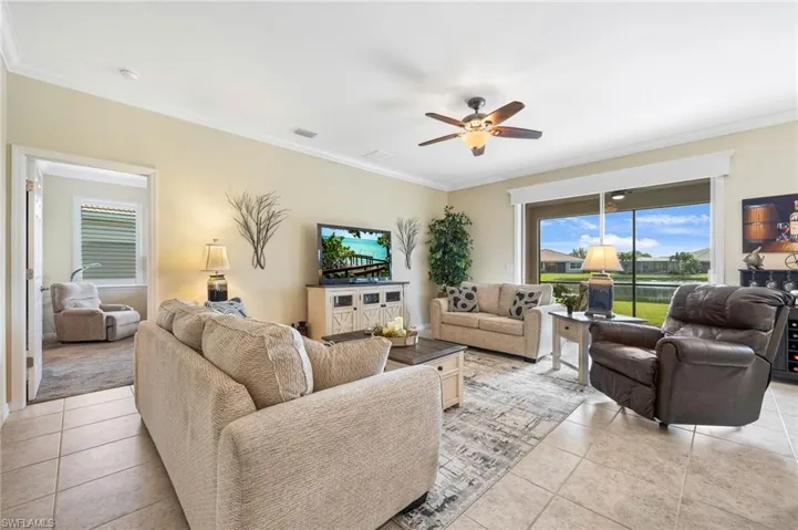 Living room with light tile floors, crown molding, and ceiling fan with water view