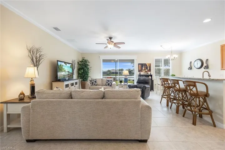 Tiled great room with lit ceiling fan, plantation shutters, and crown molding