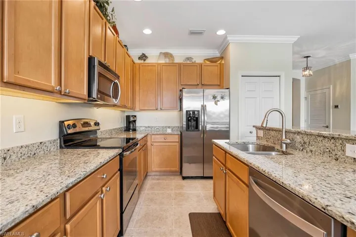 Kitchen featuring appliances with stainless steel finishes, under and above cabinet lighting, sink, light stone counters, and crown molding