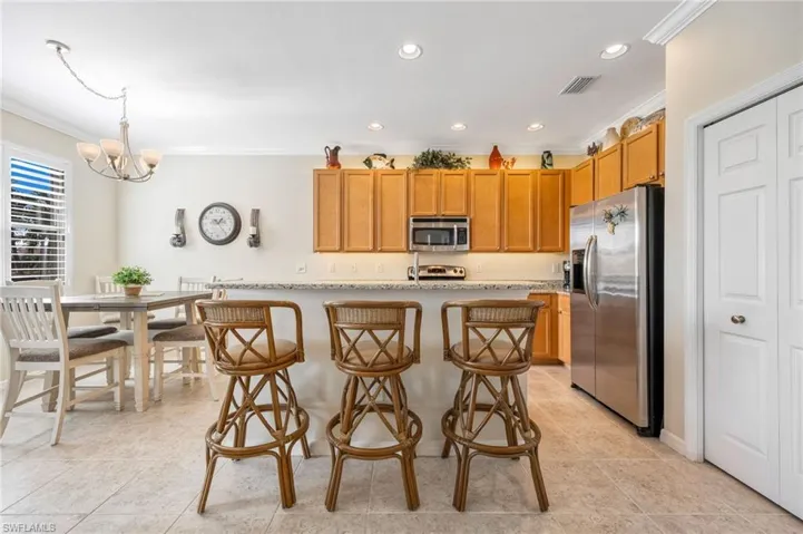 Kitchen with a breakfast bar area, stainless steel appliances, light stone countertops, an island with sink, and pantry.