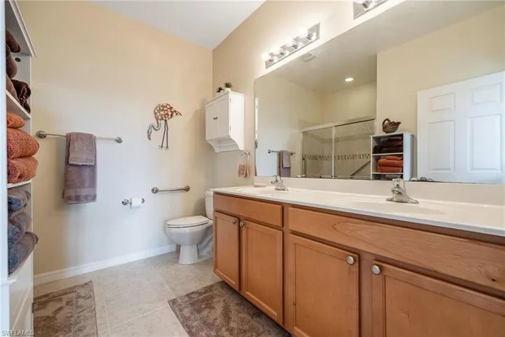 Bathroom featuring double sink vanity, toilet, tile floors, and a shower with shower door