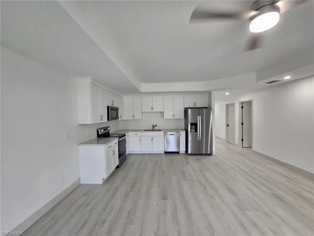 Kitchen with stainless steel appliances, white cabinetry, light wood-style floors, recessed lighting, and a raised ceiling