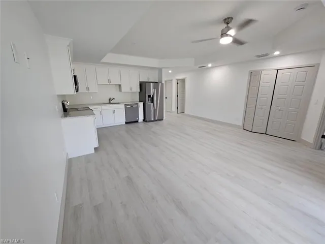 Kitchen featuring light wood finished floors, white cabinets, stainless steel appliances, open floor plan, and a ceiling fan