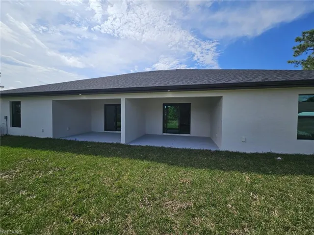 Rear view of property with stucco siding, a patio area, a yard, and a shingled roof