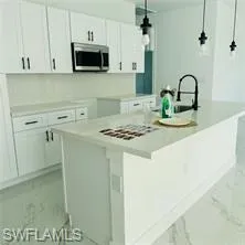 Kitchen with white cabinetry, a center island with sink, light countertops, stainless steel microwave, and decorative light fixtures