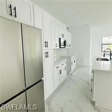 Kitchen featuring freestanding refrigerator, light countertops, white cabinets, and a center island with sink