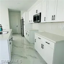 Kitchen with white cabinetry, light countertops, and light marble finish floors