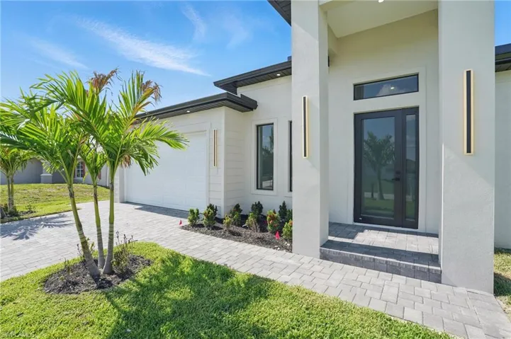 View of exterior entry featuring a garage, stucco siding, driveway, and a lawn