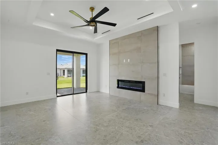 Unfurnished living room with a tray ceiling, a fireplace, baseboards, recessed lighting, and a ceiling fan