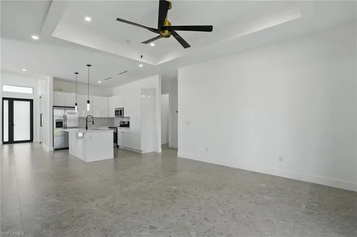 Unfurnished living room with a tray ceiling, a sink, recessed lighting, ceiling fan, and baseboards