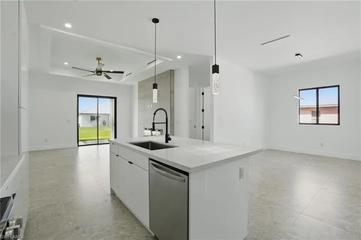 Kitchen with stainless steel dishwasher, a sink, open floor plan, a kitchen island with sink, and white cabinetry