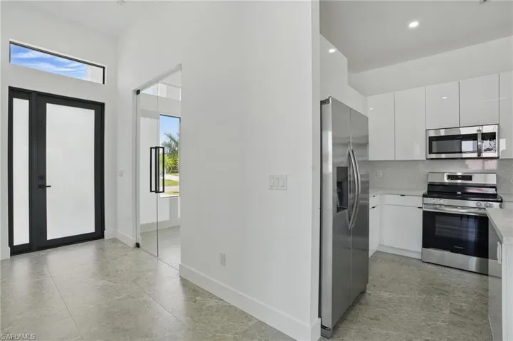 Kitchen with stainless steel appliances, healthy amount of natural light, white cabinets, light countertops, and a towering ceiling