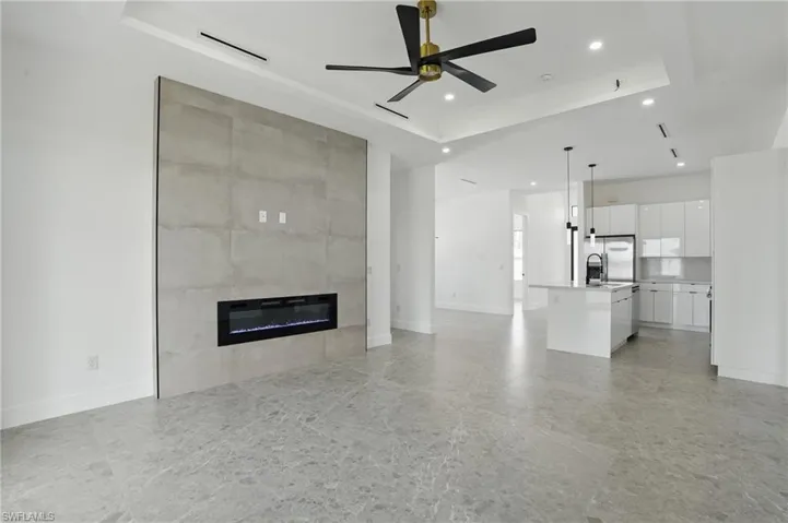 Unfurnished living room with a raised ceiling, ceiling fan, a fireplace, recessed lighting, and baseboards