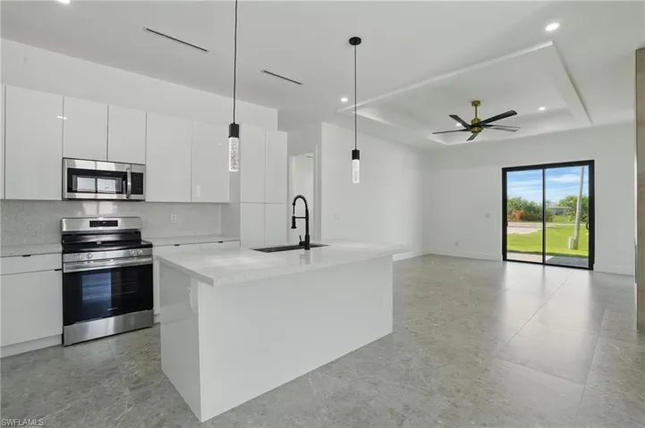 Kitchen with stainless steel appliances, a sink, white cabinetry, decorative light fixtures, and a raised ceiling