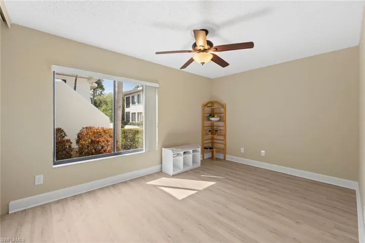 Spacious room with light wood-finish flooring, a ceiling fan with integrated lighting, and a large window