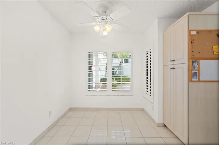 Recessed window with plantation shutters, ceiling fan with integrated lighting, and neutral square tile flooring