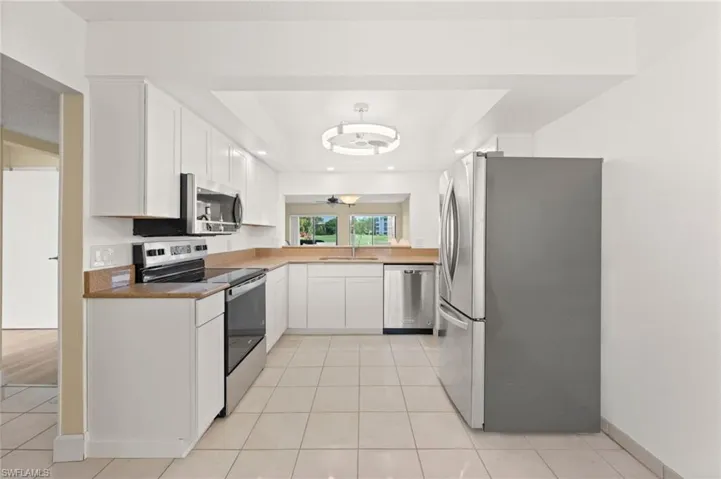 Kitchen featuring white cabinetry, light-toned countertops, tile flooring, stainless steel appliances, and a recessed ceiling with a contemporary light fixture