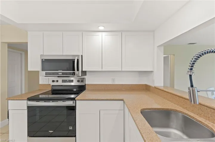 Kitchen featuring white cabinetry, stainless steel appliances, a built-in microwave, a flat-top electric range, and a stainless steel sink with a high-arch faucet