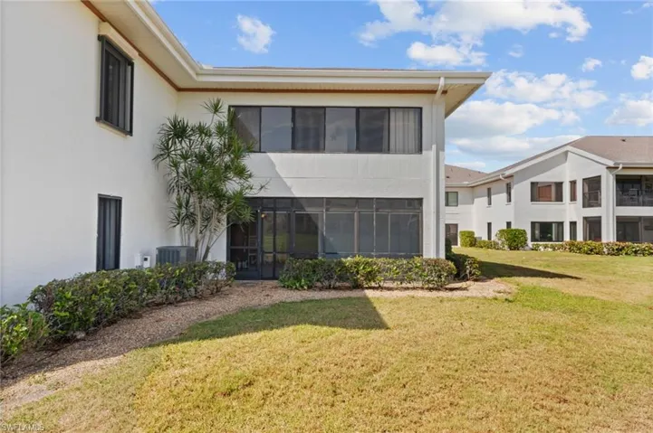 White stucco exterior featuring a screened-in patio, dark-framed windows, and a mature shrub