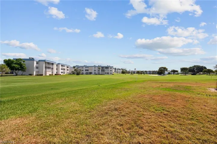 Expansive green space featuring golf course access, manicured lawns, mature trees, and multi-story residential buildings with balconies